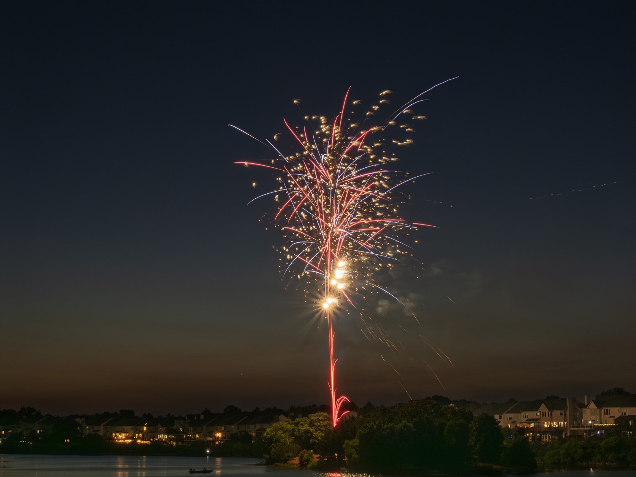 Red and blue fireworks explode in the sky in a waterfront neighborhood